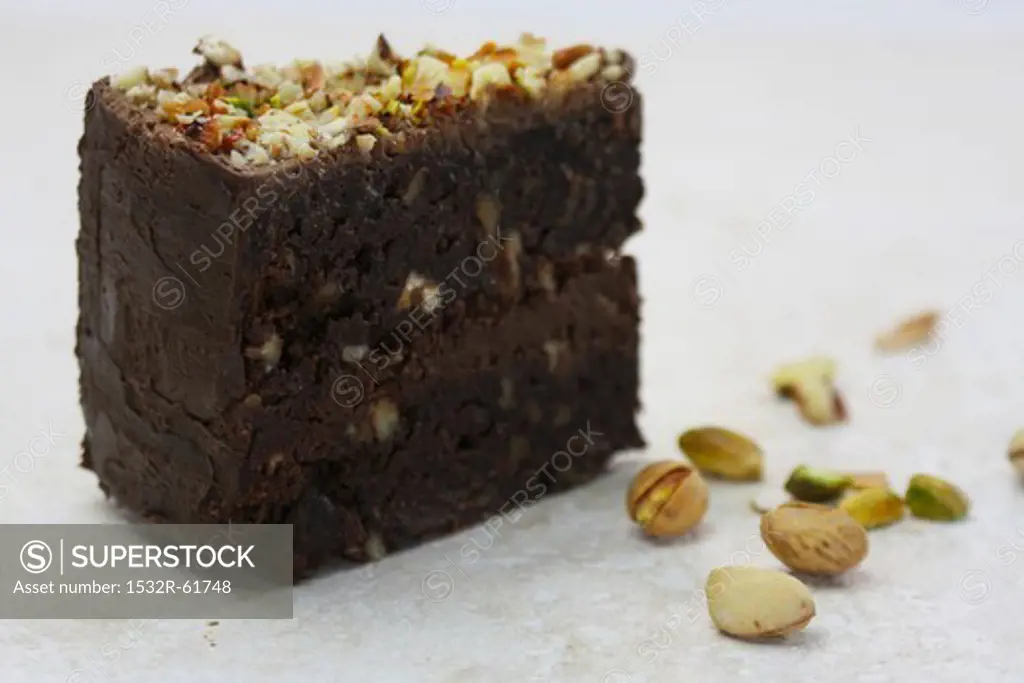 A slice of chocolate-brownie cake with nuts and pistachios
