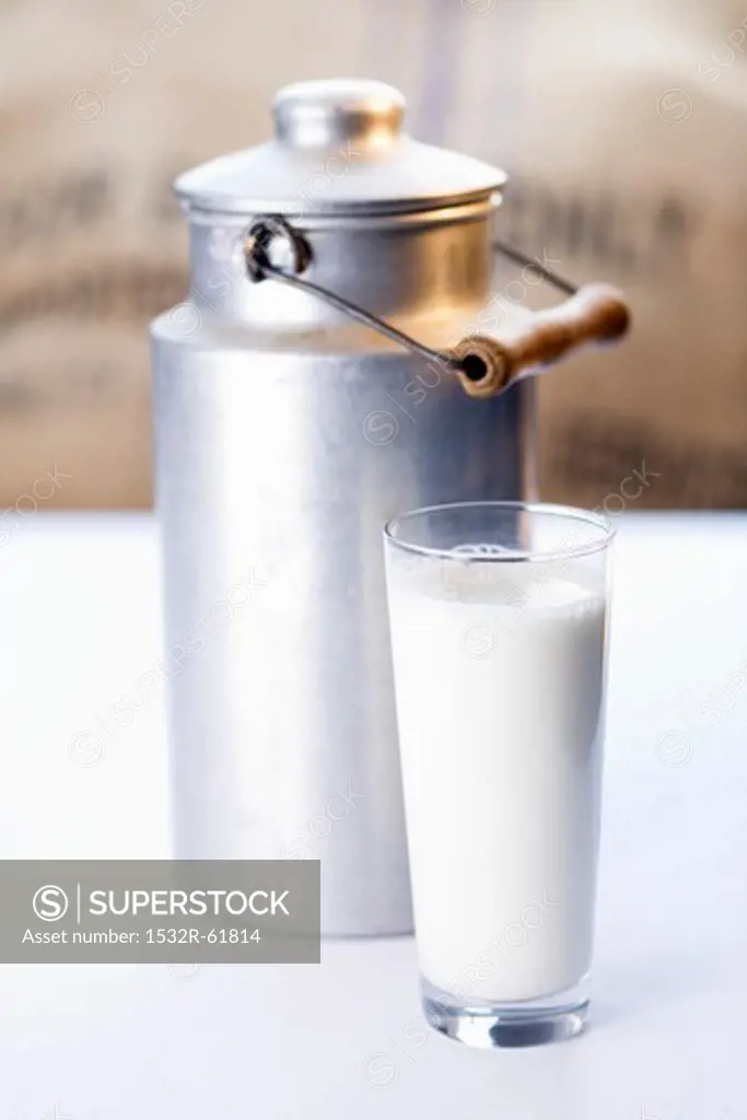A glass of milk in front of a milk can