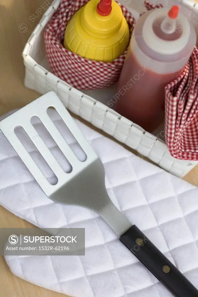 Ketchup and mustard in basket, barbecue glove, spatula