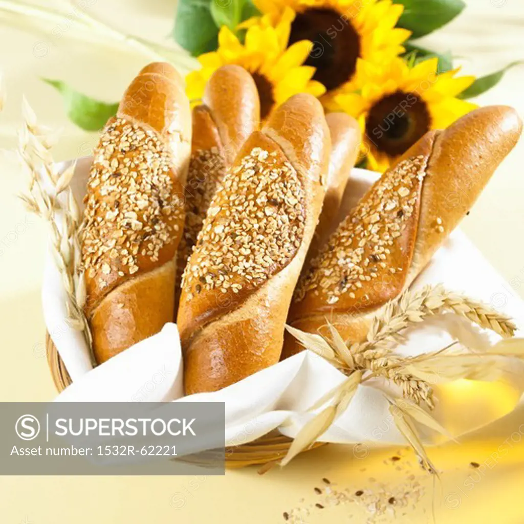 Several grain baguettes in a bread basket with sunflowers and ears of corn