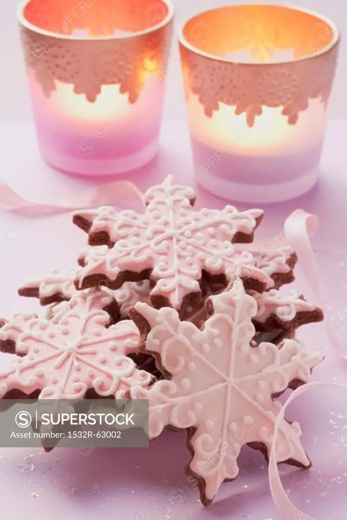 Star-shaped Christmas biscuits decorated with icing sugar with tealights in the background