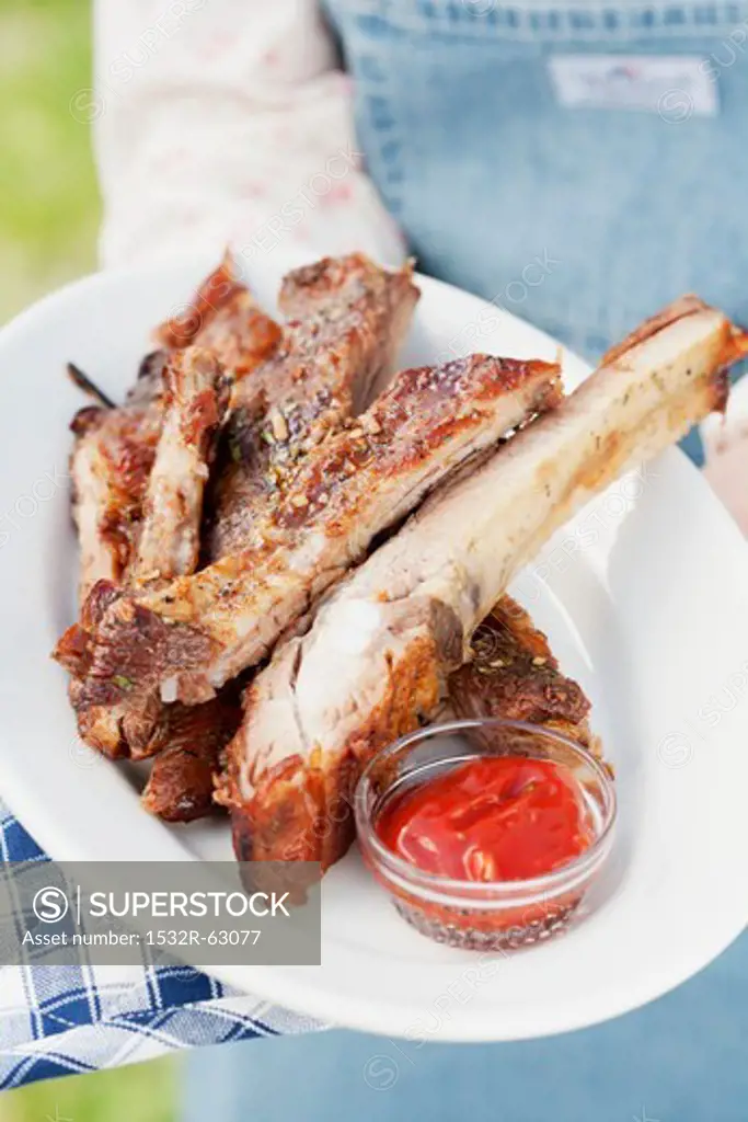 A person holding a plate of grilled spare ribs and barbecue sauce