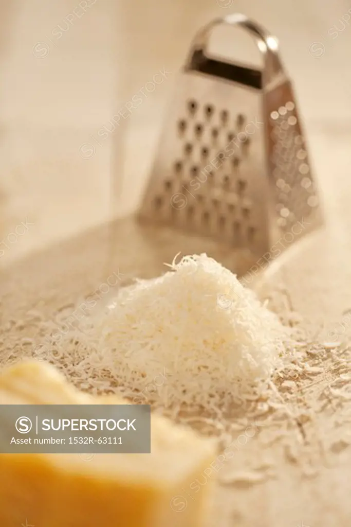 Pile of Freshly Grated Parmesan Cheese with Cheese Grater; Wedge of Parmesan Cheese