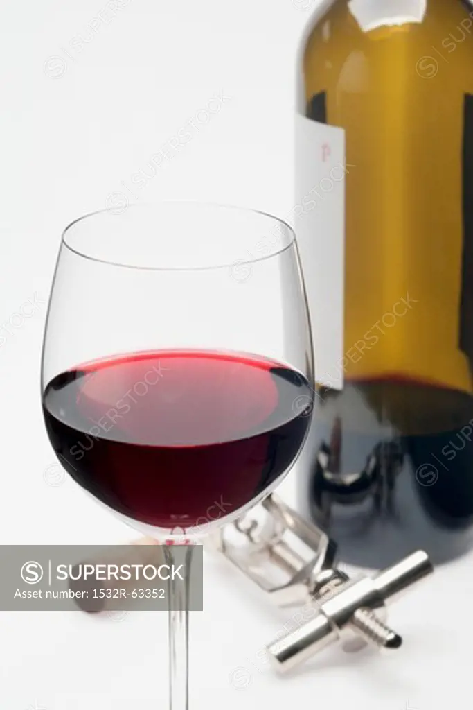 A glass of red wine, cork, corkscrew and bottle of red wine