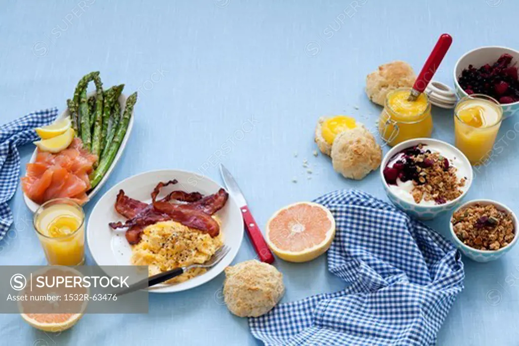 A breakfast table laid with scrambled egg and bacon, salmon, jam, muesli and grapefruit
