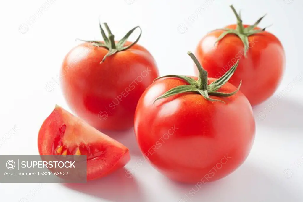 A slice of tomatoes and three whole tomatoes