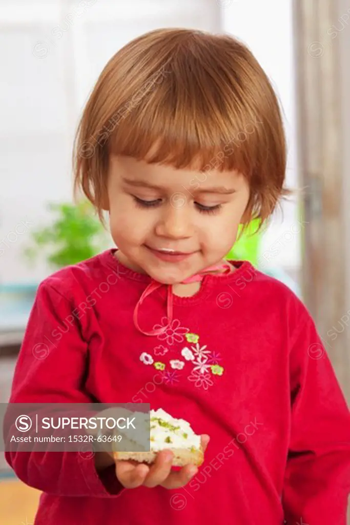 A little girl holding a slice of bread topped with cottage cheese