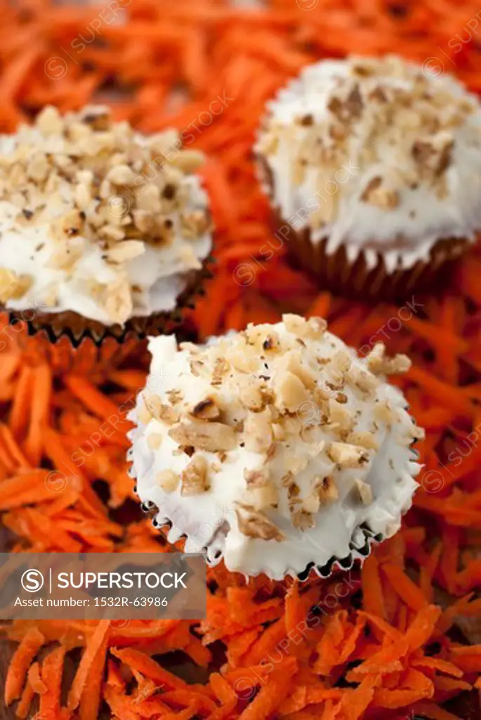 Three Carrot Cake Cupcakes with Cream Cheese Frosting and Walnuts; On Shredded Carrots