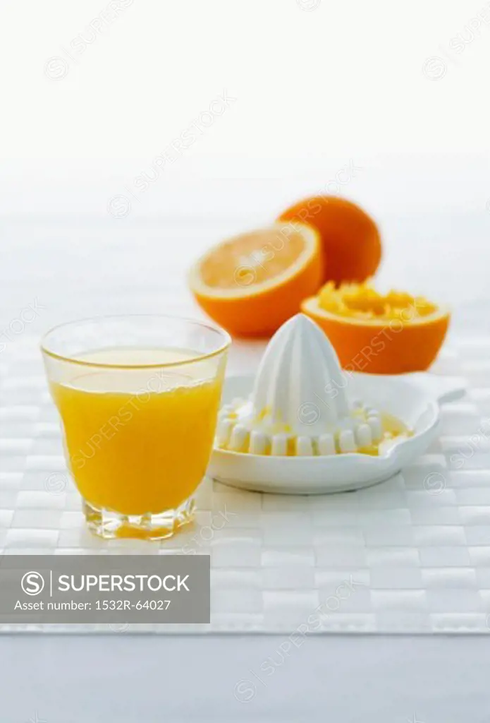 A glass of orange juice, citrus squeezer and oranges