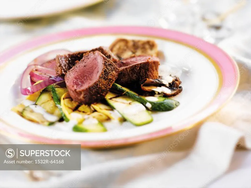 Three Slices of Lamb Loins with Steamed Vegetables on a White Plate with a Pink Rim