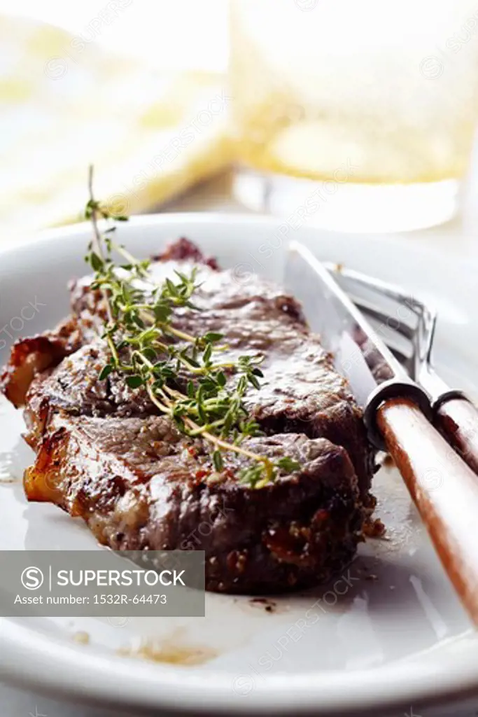 Steak with a Sprig of Oregano on a Plate with Fork and Knife