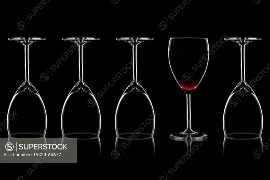 Row of wine glasses and a glass of red wine against a black background