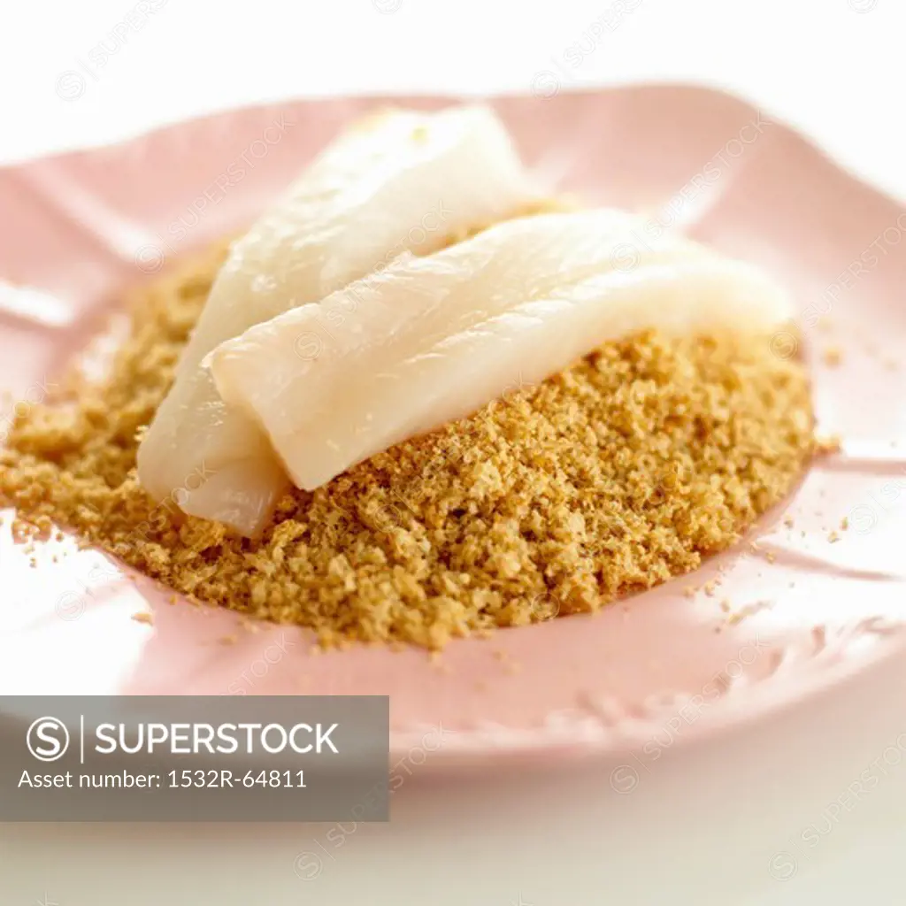 Raw fish fillets on a pile of breadcrumbs
