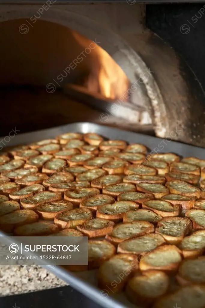 Baked Baguette Slices on a Sheet Pan Coming Out of a Pizza Oven