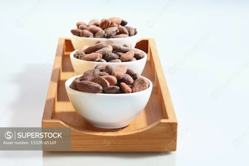 Three bowls of cocoa beans on a wooden board
