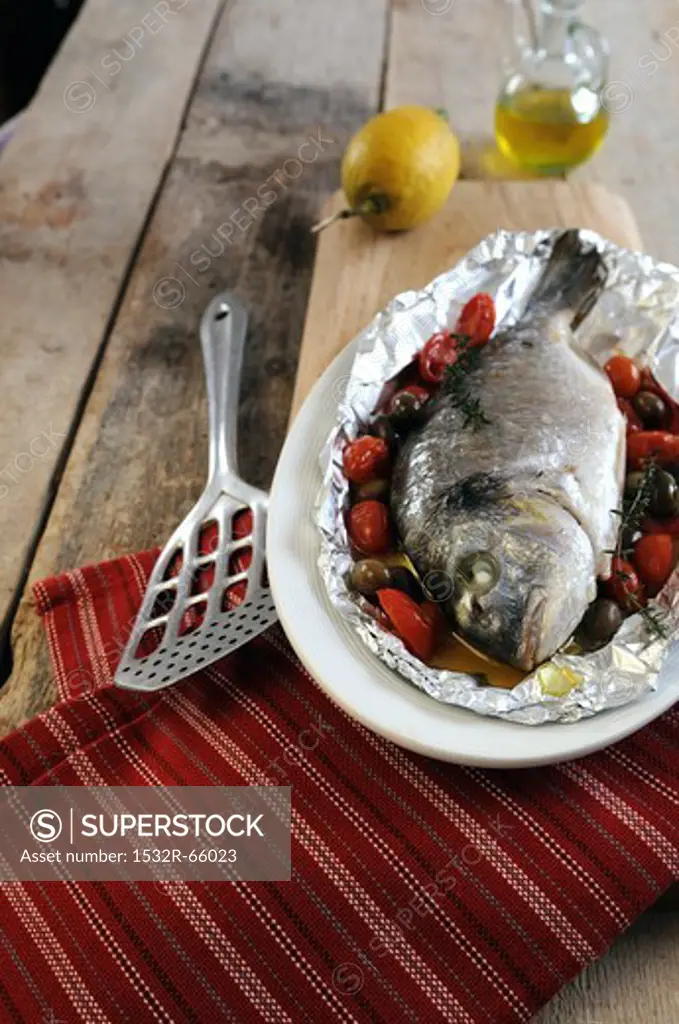 Oven roasted porgy wrapped in foil with cherry tomatoes and olives