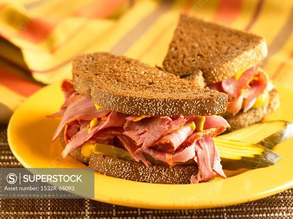 Corned Beef Sandwich with Mustard and Pickles on Pumpernickel Bread; Halved on a Yellow Plate