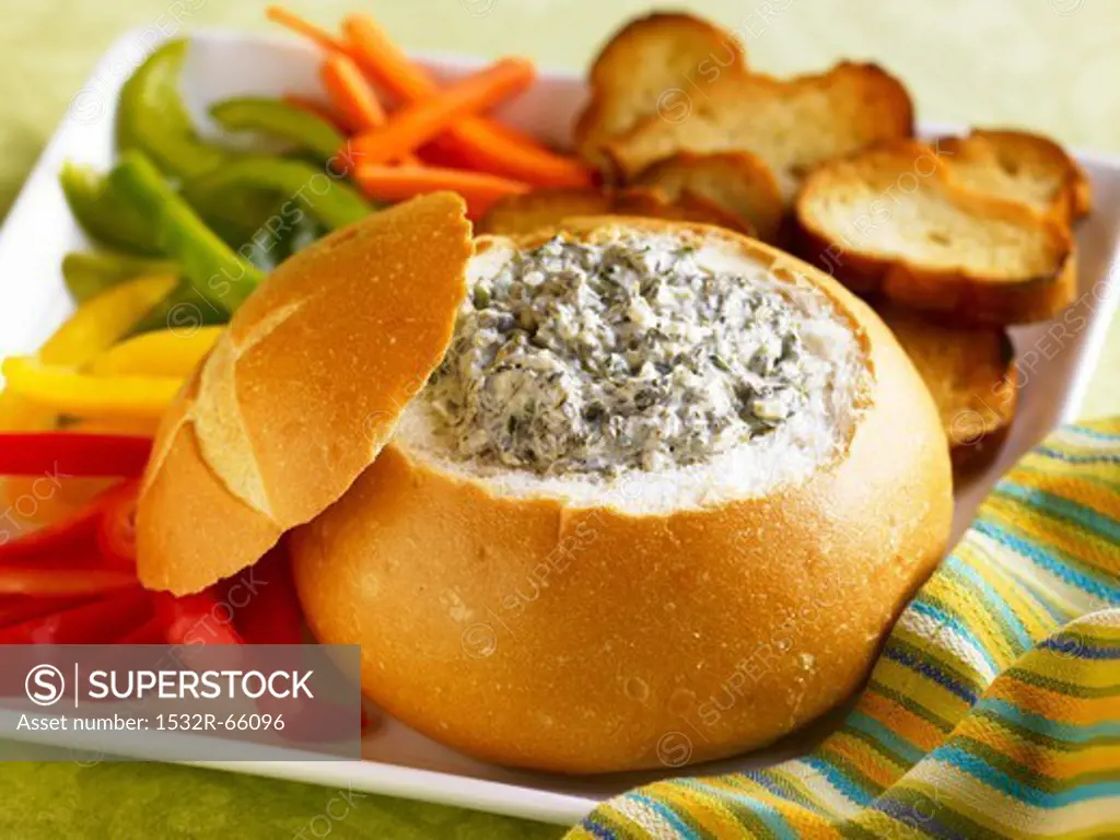 Spinach Dip in a Bread Bowl with Sliced Veggies and Toasted Bread Slices for Dipping