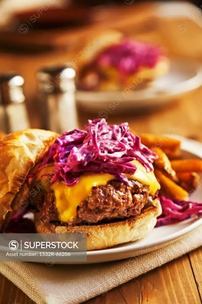 A Cheeseburger topped with red cabbage cole slaw on a plate with french fries