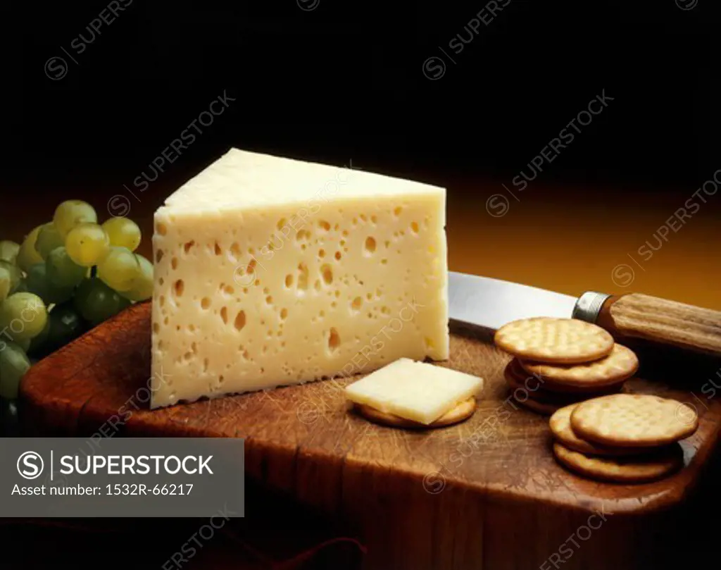 Baby Swiss Cheese Wedge on a Cutting Board with Crackers and Green Grapes