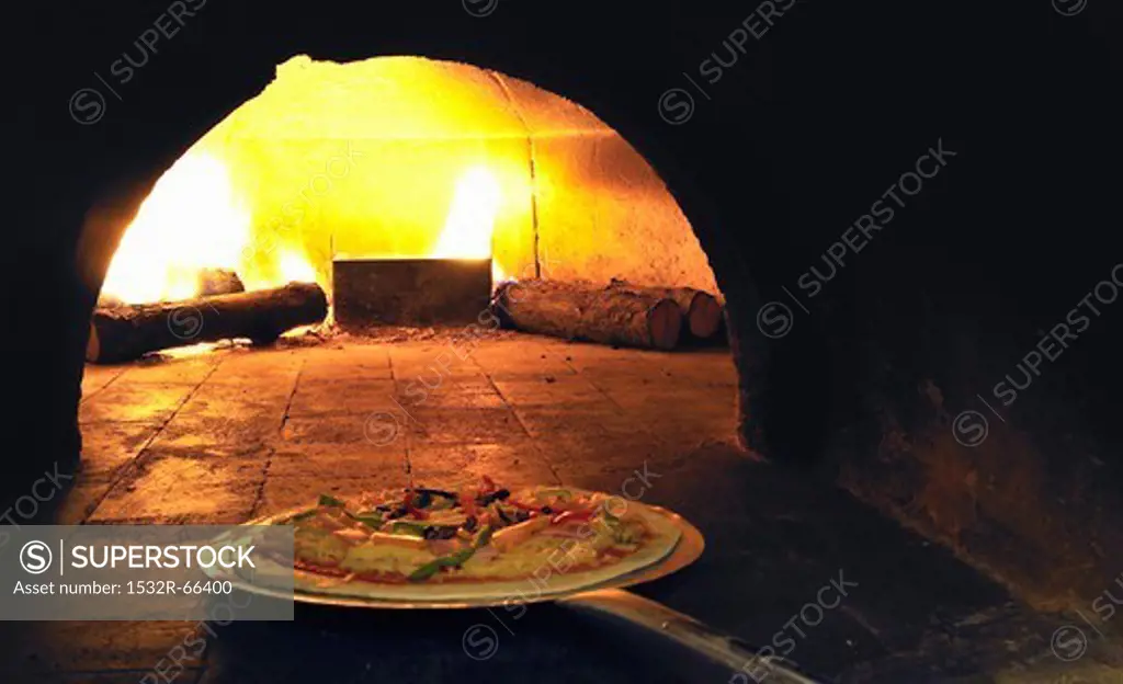 A pizza being placed in a wood-fired oven