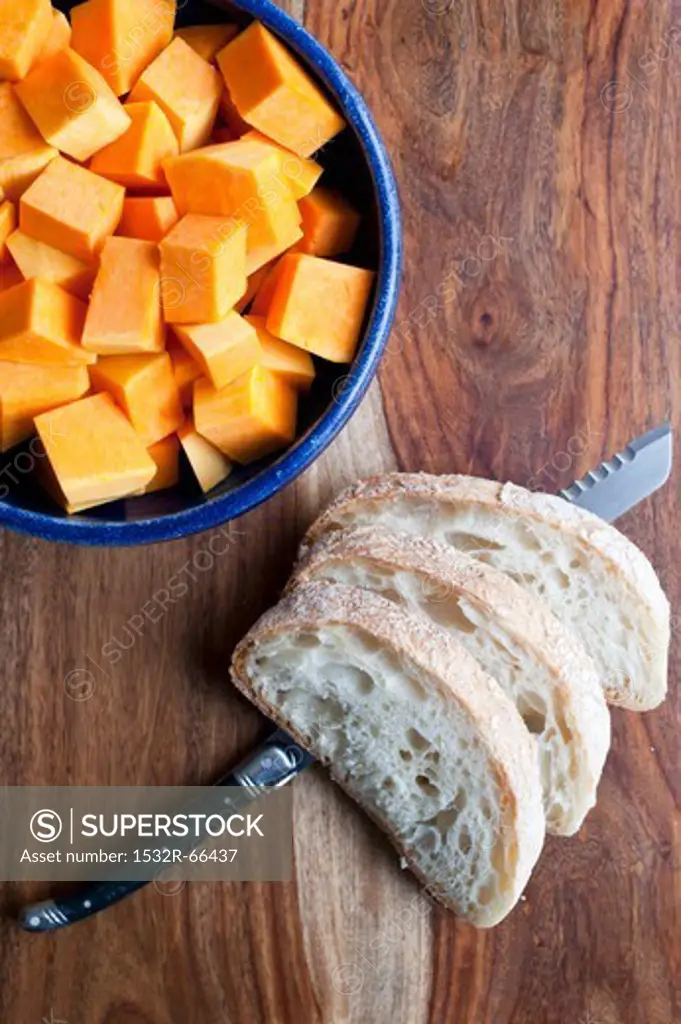 Peeled and Cubed Butternut Squash in a Bowl; Slices of Bread with a Knife