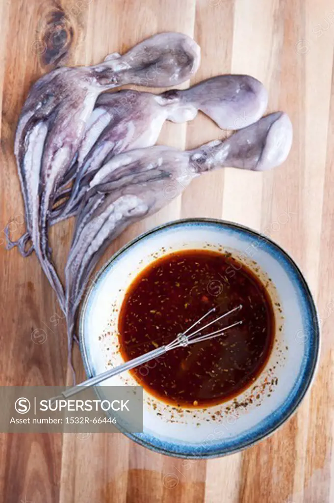 Three Raw Baby Octopus with a Bowl of Marinade on a Cutting Board