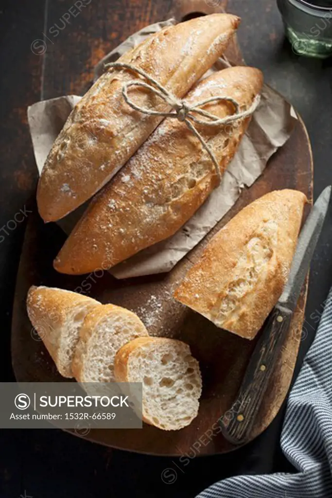 Small baguette rolls, whole and sliced, on a wooden board