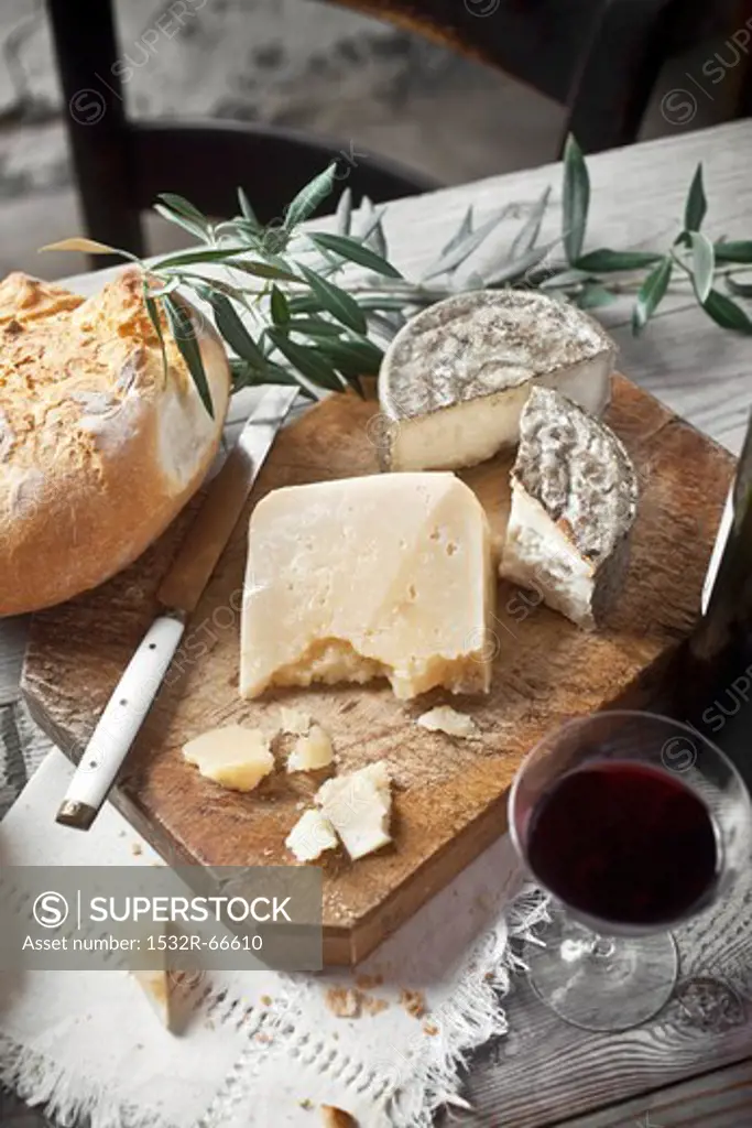 Manchego cheese and goat's cheese on a wooden board with bread and red wine