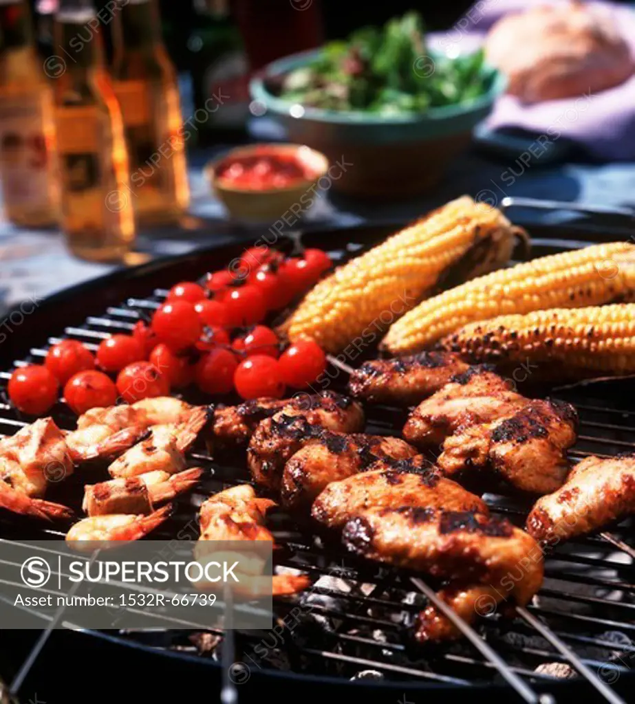 Chicken wings, prawn skewers, baby sweetcorn and tomatoes on the barbecue grill