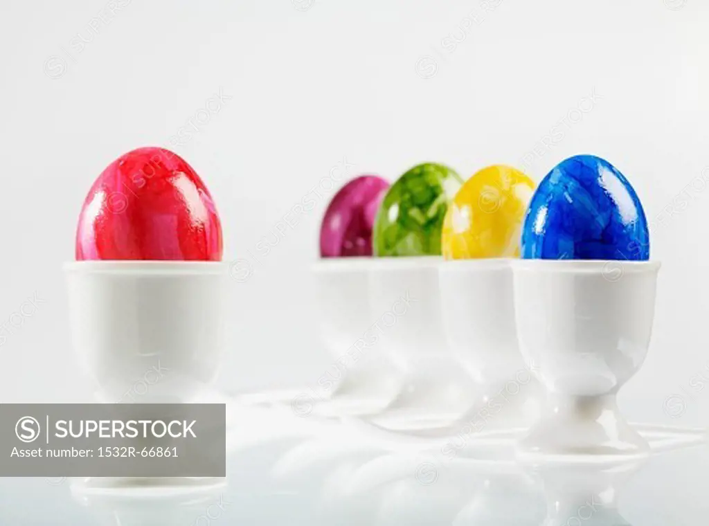 Five eggs, brightly coloured for Easter, in white eggcups with egg spoons