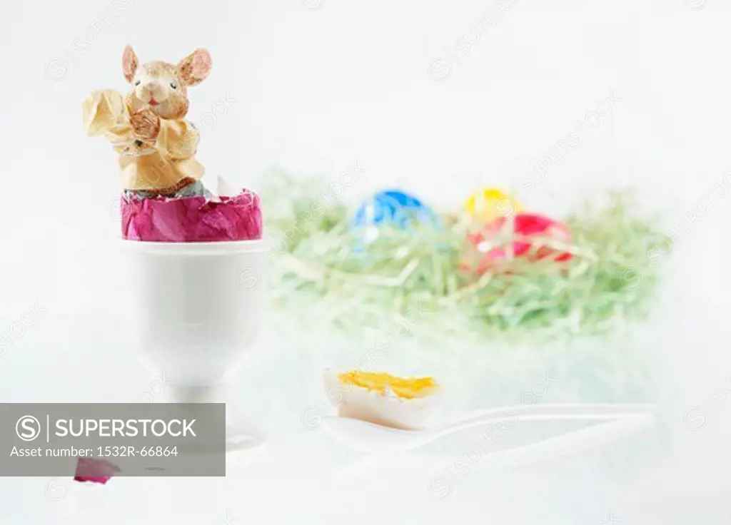 An Easter bunny figurine in a boiled egg with the top cut off, with an Easter nest of colourful eggs in the background
