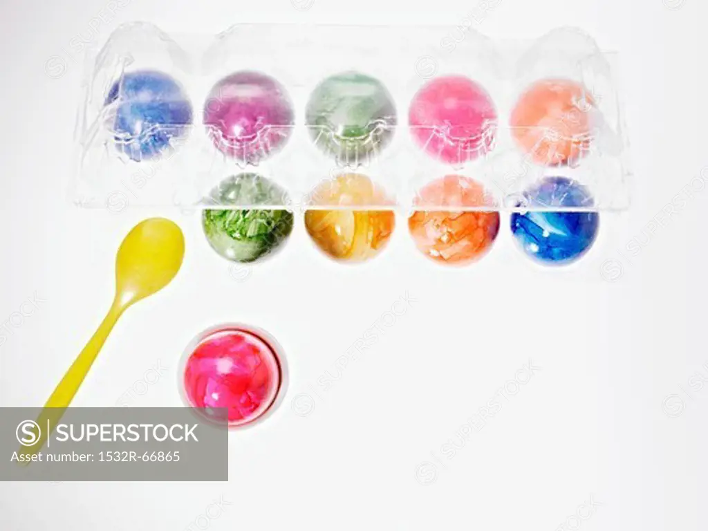 Brightly coloured eggs in an eggcup and in a transparent egg box