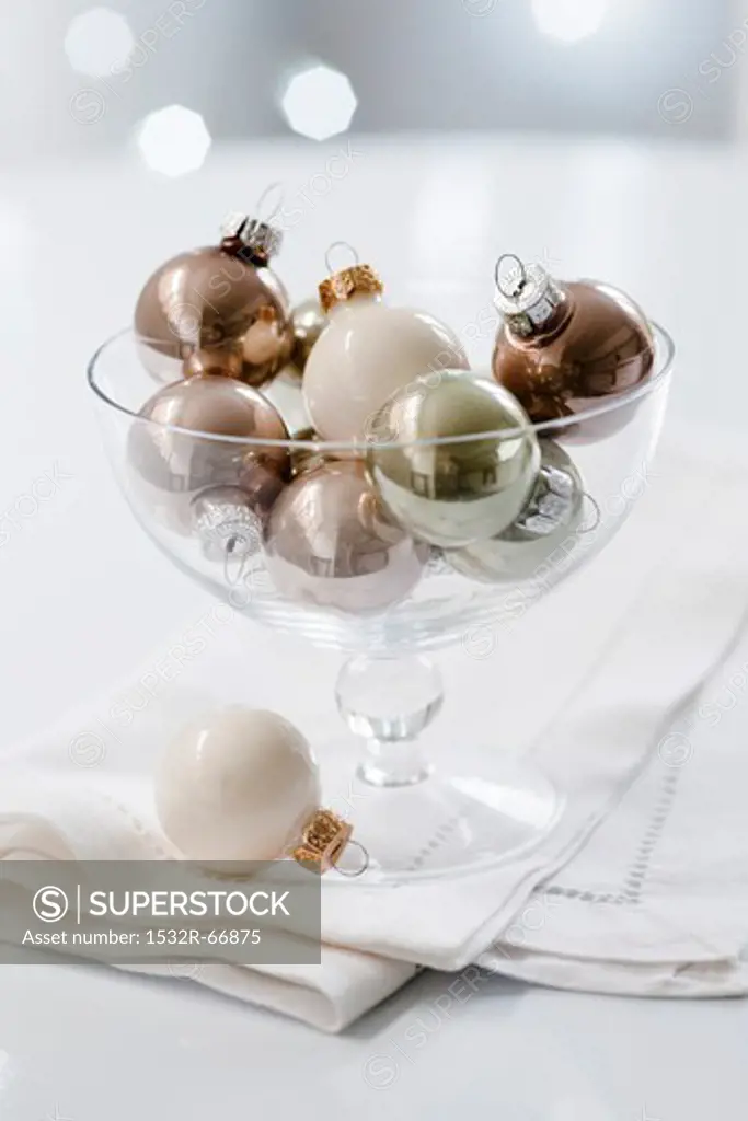 White, gold and silver Christmas tree baubles in a glass dish