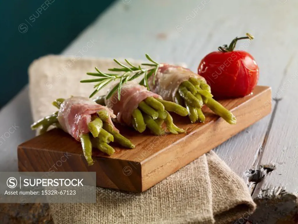 Green beans wrapped in bacon with rosemary on a small wooden board