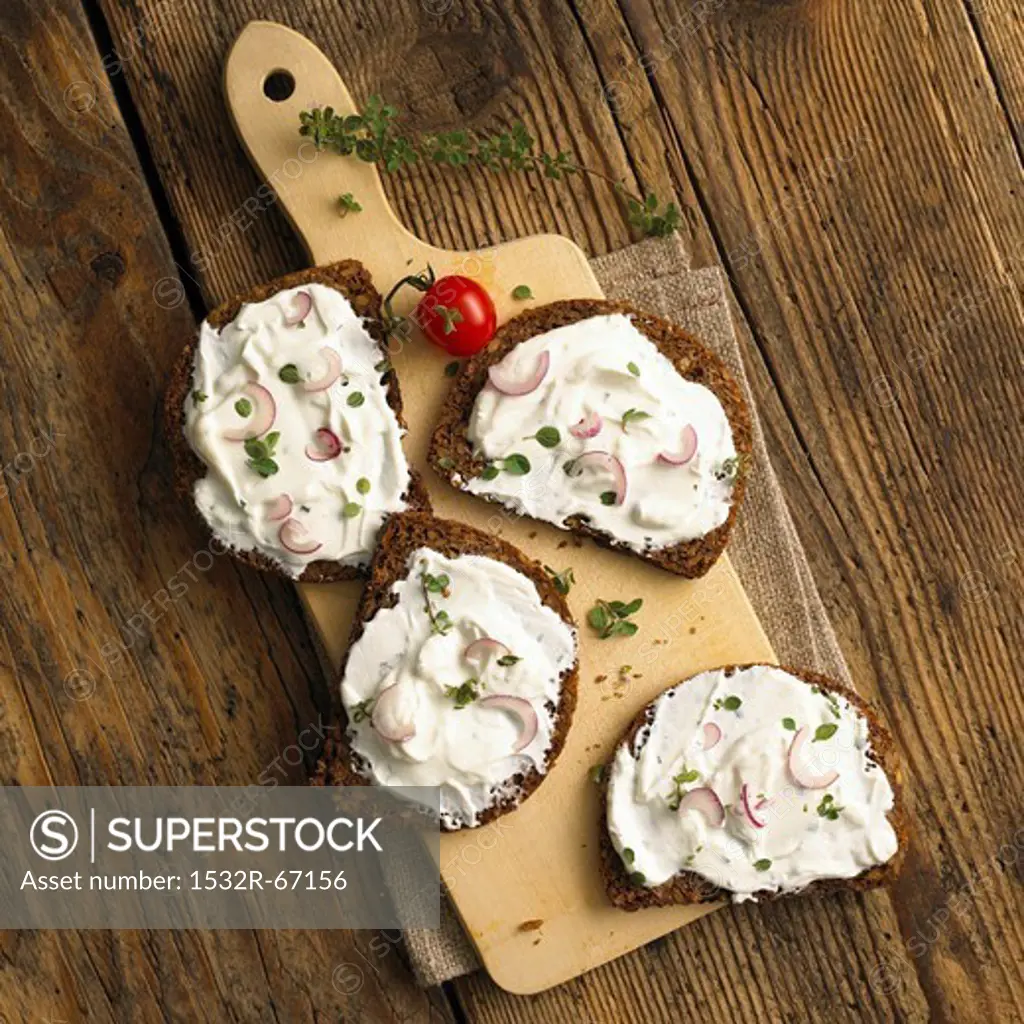 Slices of whole grain bread with quark and onions on a wooden board (top view)