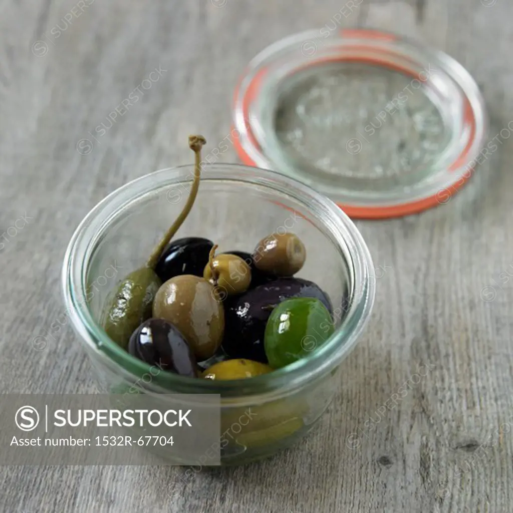 Assorted Olives in a Small Jar; Opened on a Wooden Surface