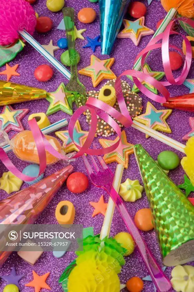 overview still life of various party decorations, party poppers sweets and straws for the party table on a purple glittery table