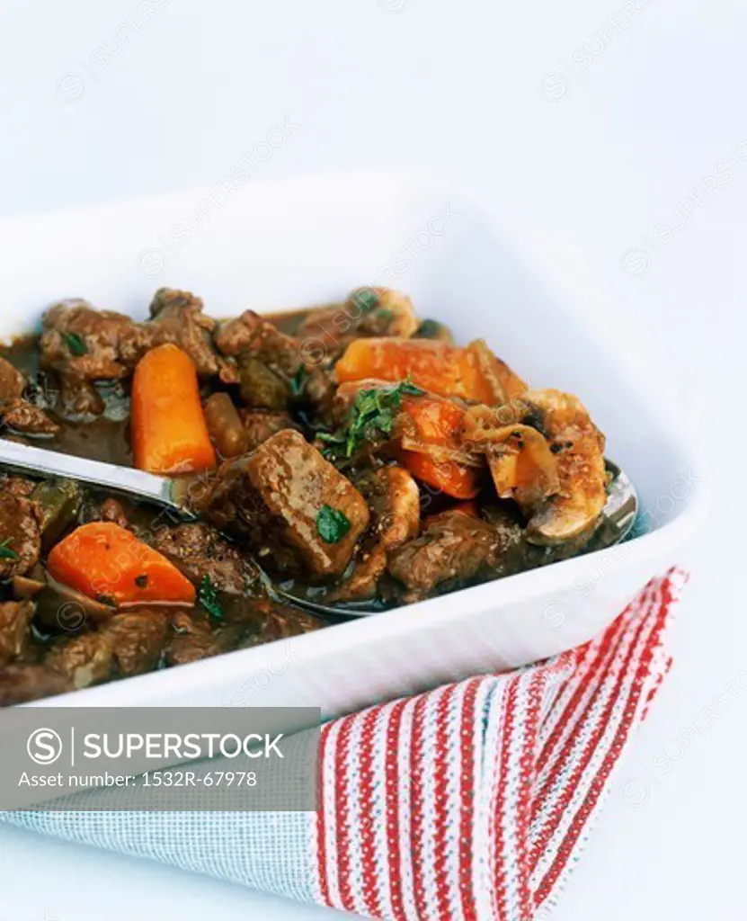 beef casserole with carrots in a white dish with stripy tea towel white cut out