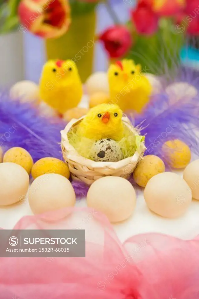still life arrangement of Easter simnel cake with pink chiffon ribbon and yellow chicks with spring tulips