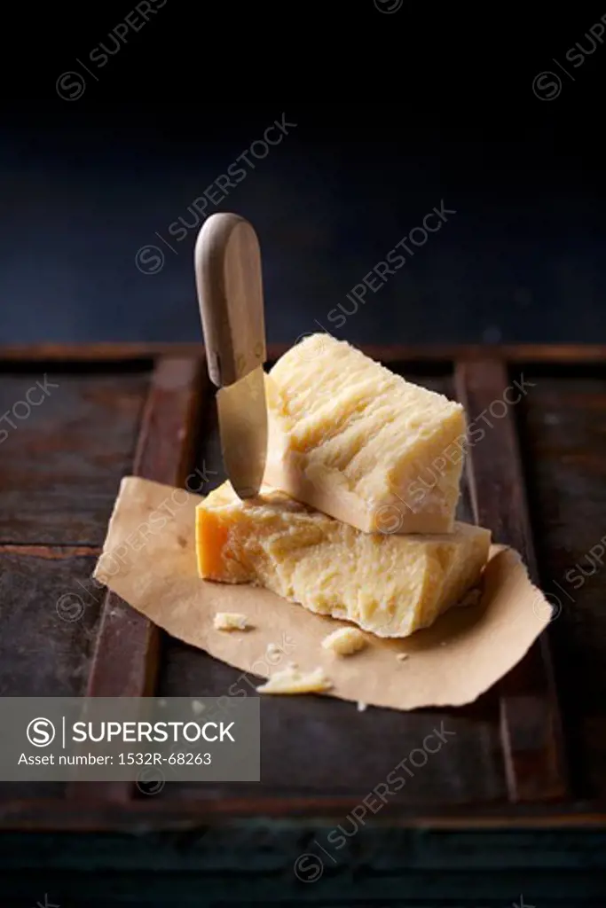 Stacked chunks of parmesan on dry flatbread, with a cheese knife stuck into one of the chunks of cheese