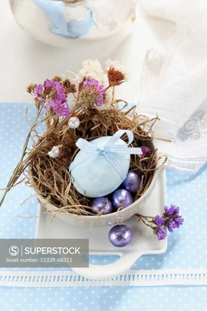 An egg decorated with a ribbon, dried flowers and chocolate eggs in an Easter nest made of moss and grass