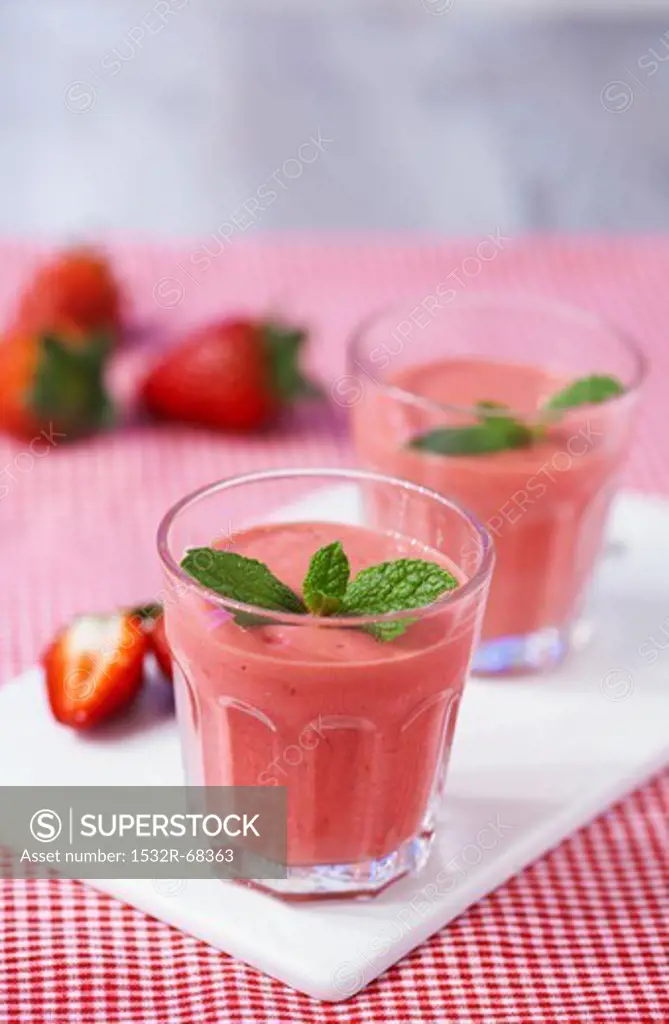 Strawberry smoothies topped with mint leaves on a chopping board on a red gingham tablecloth