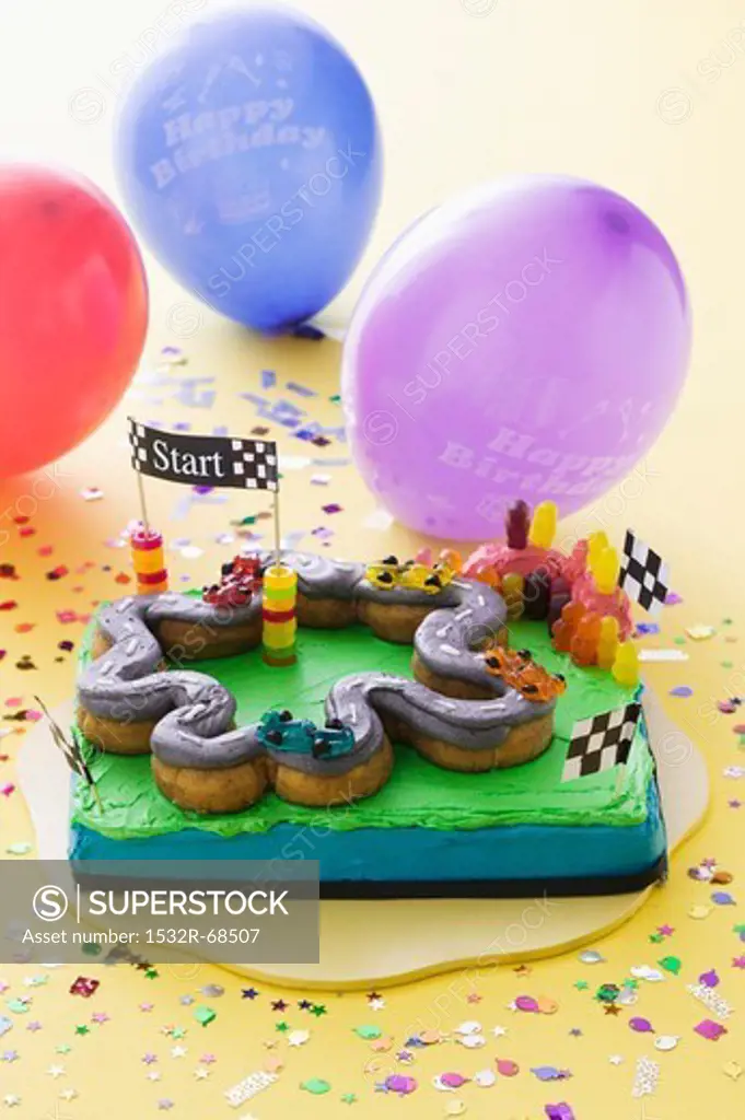 A child's birthday cake (a racing track) and balloons