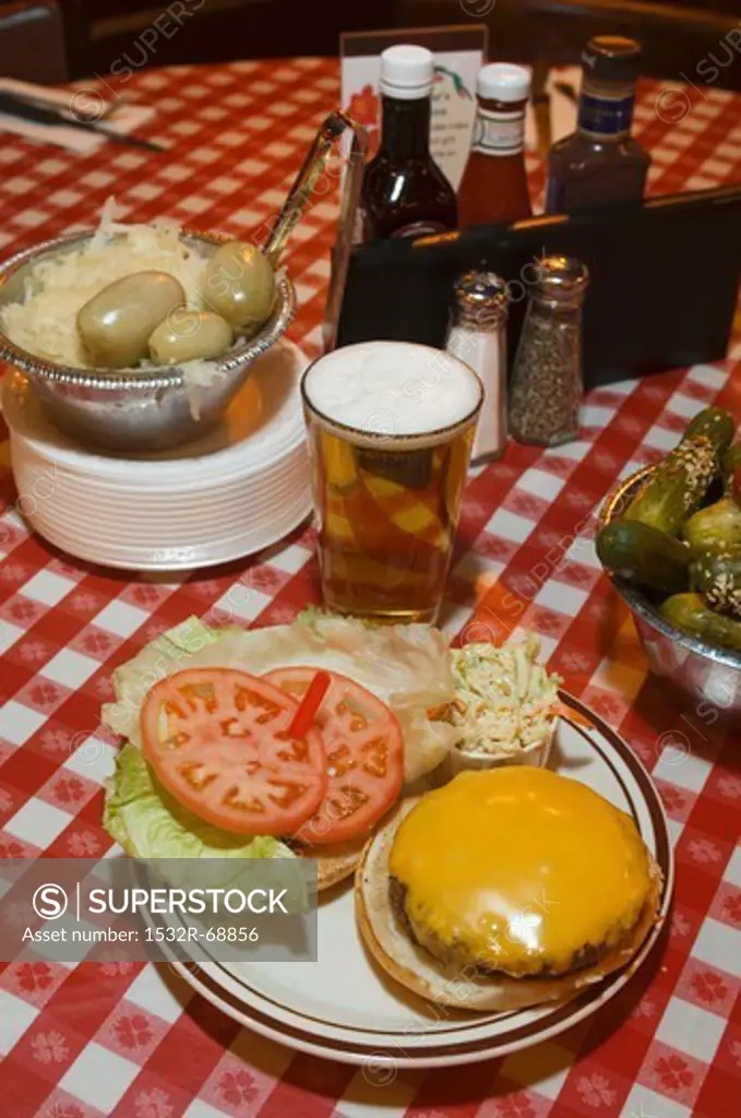 A cheeseburger, beer and pickled gherkins on a checked tablecloth