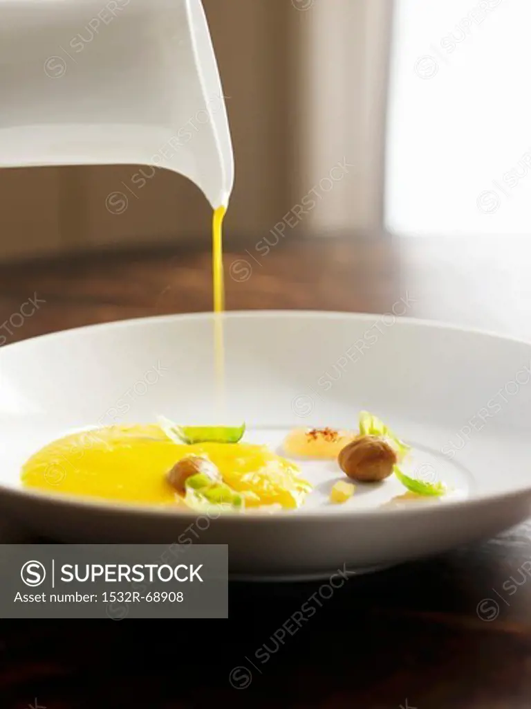 Pouring Smooth and Creamy Squash Soup into a White Bowl with Garnishes
