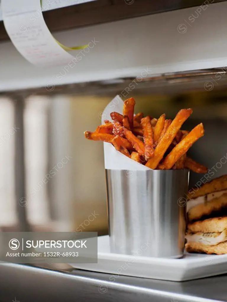 Seasoned Fries with Wax Paper in a Steel Cup on a Restaurant ""Order-Up"" Counter