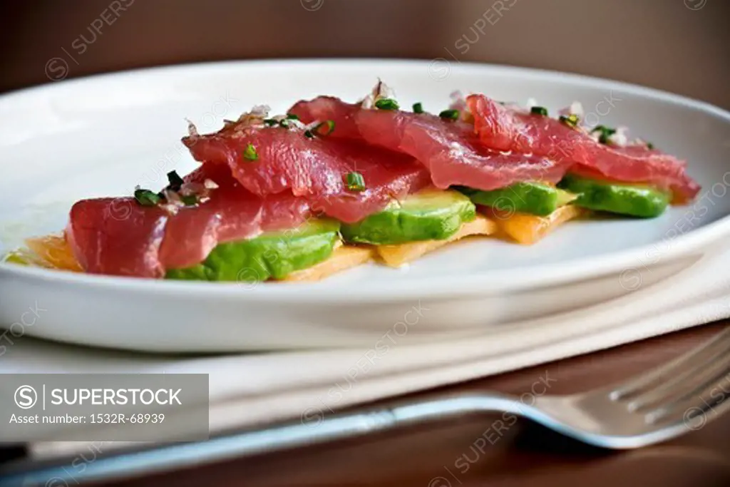 Raw Tuna Slices Over Sliced Avocado on a White Plate