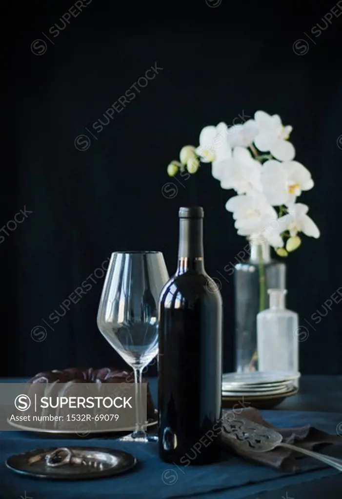 Wine Bottle, Wine Glass and a Whole Chocolate Bundt Cake; White Flowers in the Background