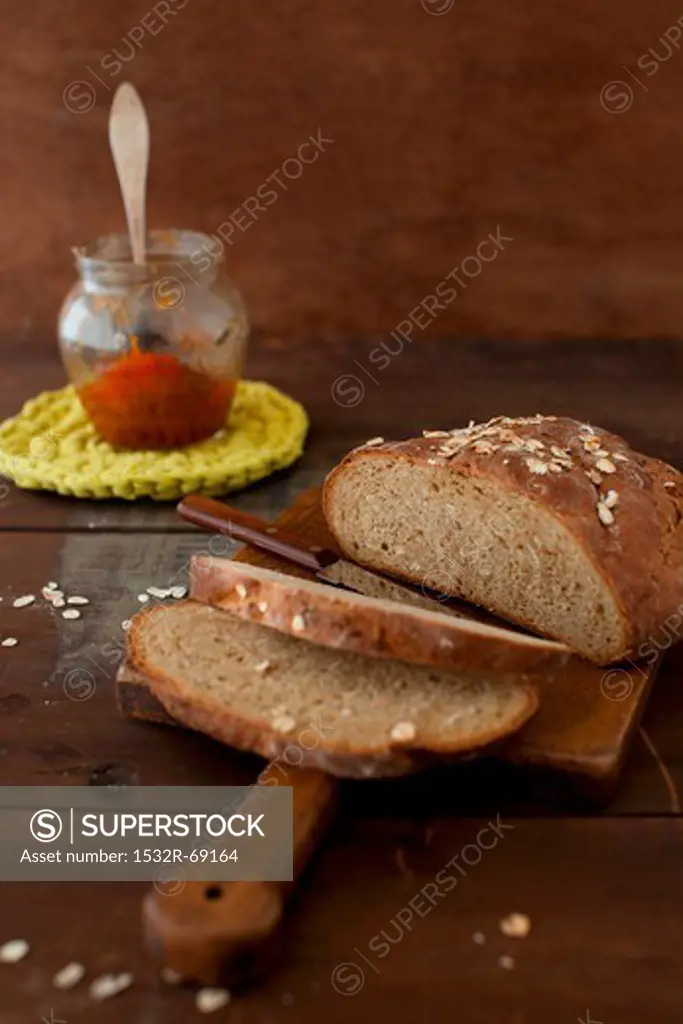 Partially Sliced Loaf of Oat Bread on a Cutting Board; Jar of Jam